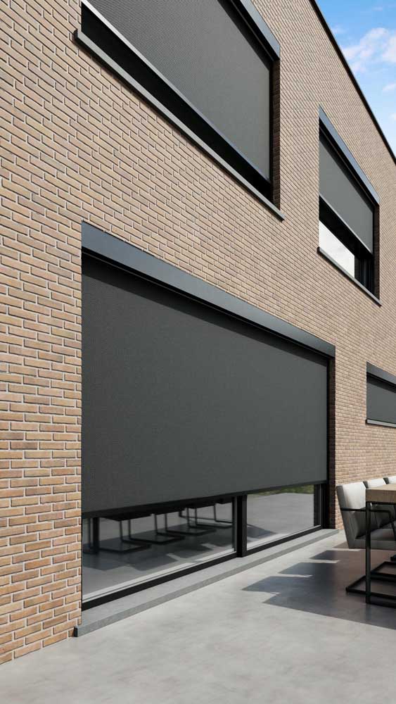 Bakstenen gevel met donkere zip-screens voor grote ramen, deels neergelaten